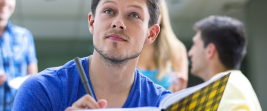 Ein Junger Mann der nach oben schaut und ein Buch und ein Stift in der Hand hält