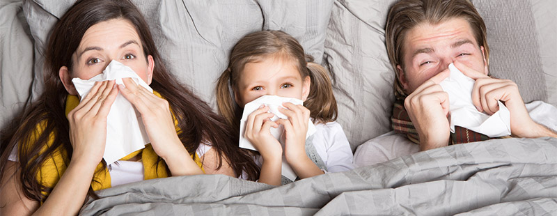 3 Kranke Personen die im Bett liegen und ein Taschentuch vor der Nase haben
