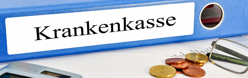 Ein Bild auf dem mehrere Unterlagen liegen ebenso ein Blauer Ordner mit dem Vermerk Krankenkasse eine Brille und einen Taschenrechner. Neben der Brille liegt Kleingeld