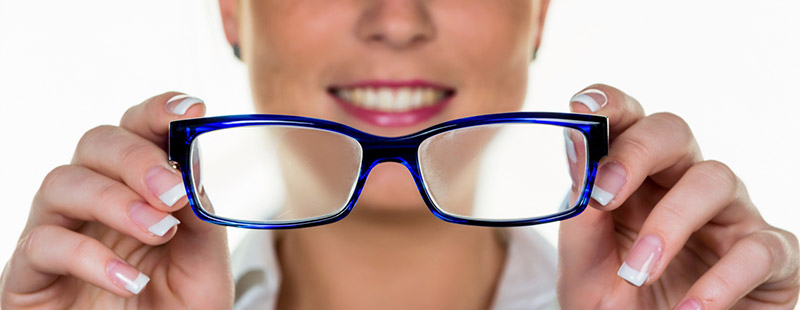 Eine Dame die in den Vordergrund eine Brille hält und lächelt