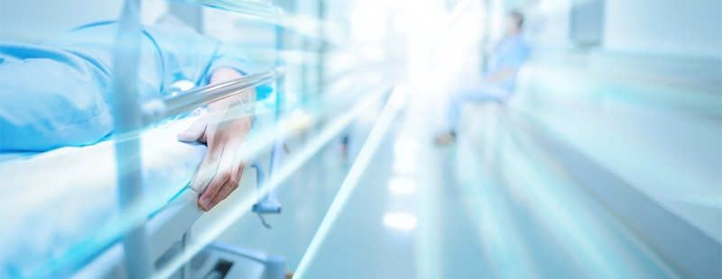 Ein Bild in Blau auf dem eine Person im Krankenbett liegt und im Hintergrund eine weitere Person auf einer Wartebank sitzt