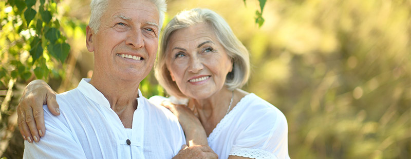 Ein Bild wo ein älteres Pärchen im Grünen sitzt und sich im Arm halten