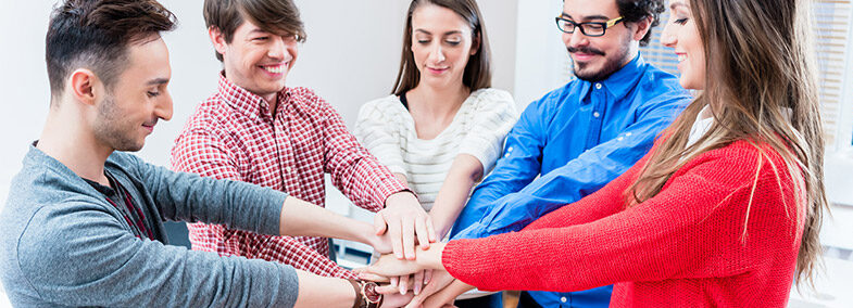 5 Personen die die Arme in einem Kreis ausstrecken und Ihre Hände aufeinander halten.