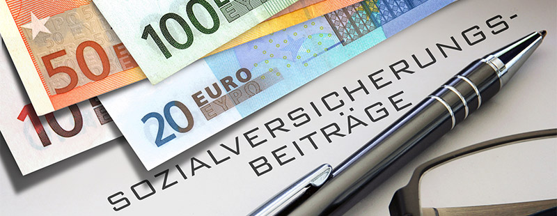 4 verschiedene Geldscheine und ein Kugelschreiber die auf einem Blatt liegen mit dem Hinweis auf Sozialversicherungsbeiträge