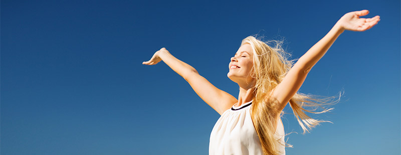 Eine blonde Frau mit ausgestreckten Armen die mit geschlossenen Augen in die ferne blickt