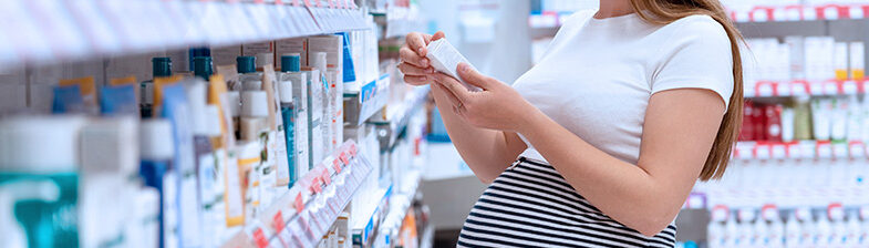 Eine Schwangere Frau die vor einem Medikamenten Regal steht und ein Medikament in der Hand hält