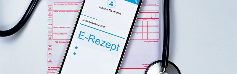 Ein Bild mit einem Rezept, auf dem Rezept liegt ein Handy mit dem Hinweis E-Rezept